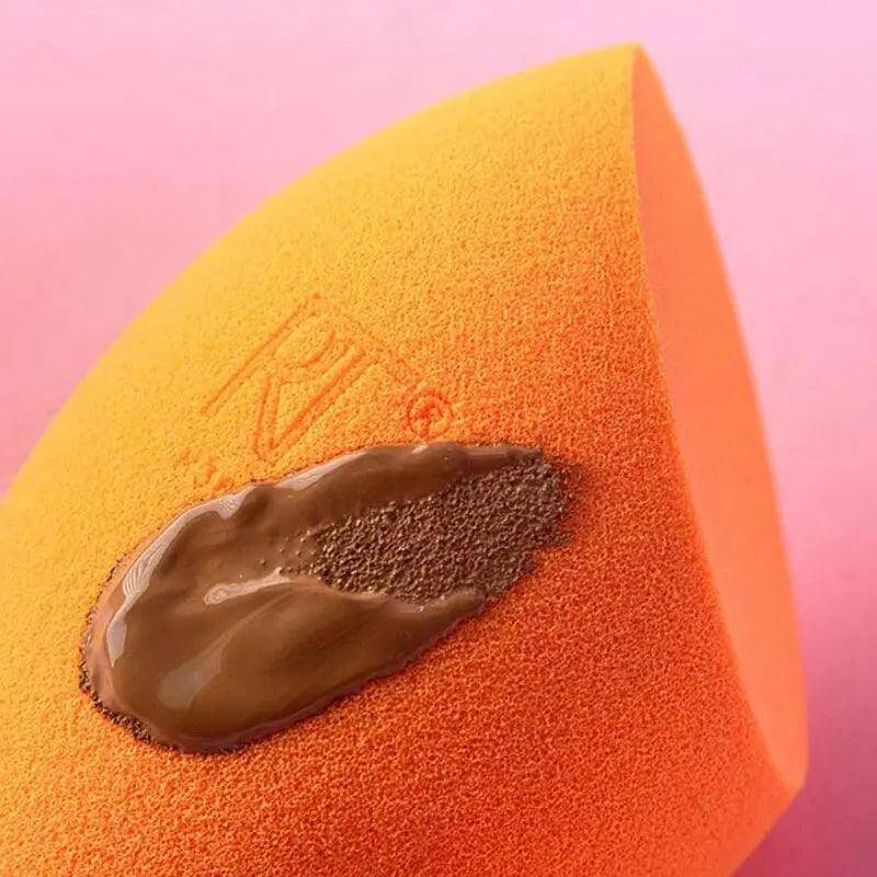 Real Techniques Miracle Complexion Sponge with liquid foundation on top against a pink background.