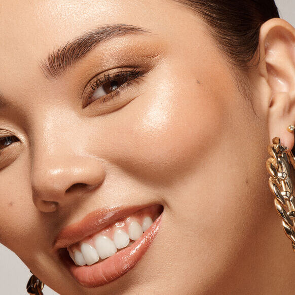 Close-up of a woman smiling with glowing skin, showcasing healthy radiance and VIEVE Skin Dew liquid highlighter.