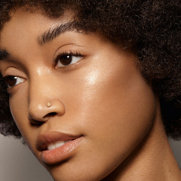 Close-up of a woman showcasing glowing skin, enhanced by VIEVE Skin Dew highlighter, promoting radiant beauty.
