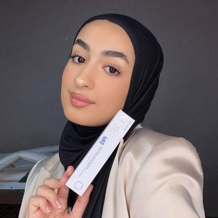Woman in a hijab holding XLash Eye Lash Serum Pro 6ml, showcasing fuller, longer lashes in 28 days.